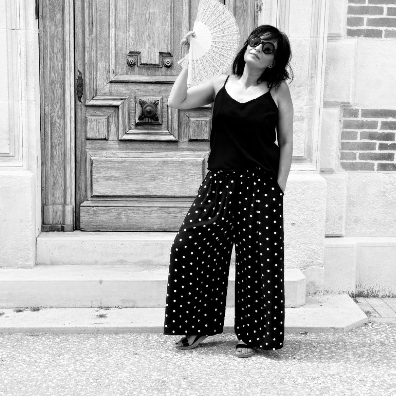 Femme en tenue noire et pois élégante devant une porte en bois, style minimaliste et intemporel