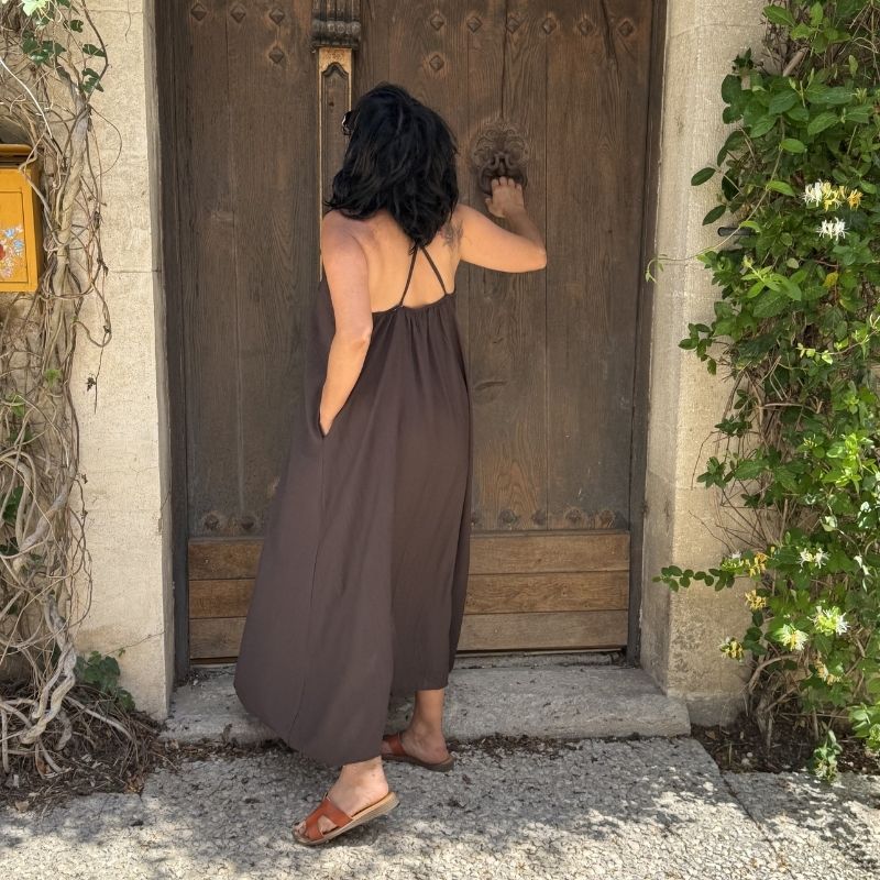 Femme en robe fluide marron devant une porte en bois, ambiance naturelle et authentique